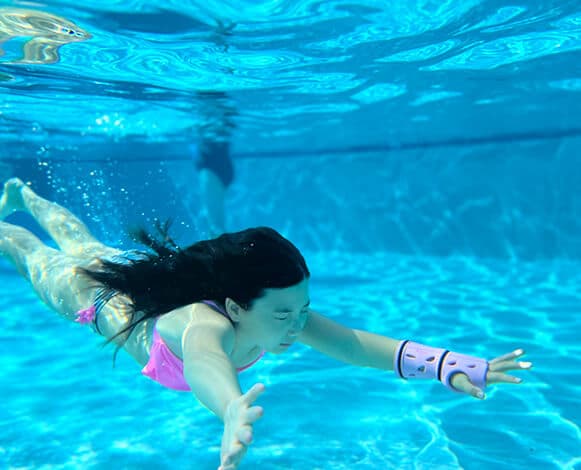 Girl wearing a 3D printed cast on her wrist swimming in a pool